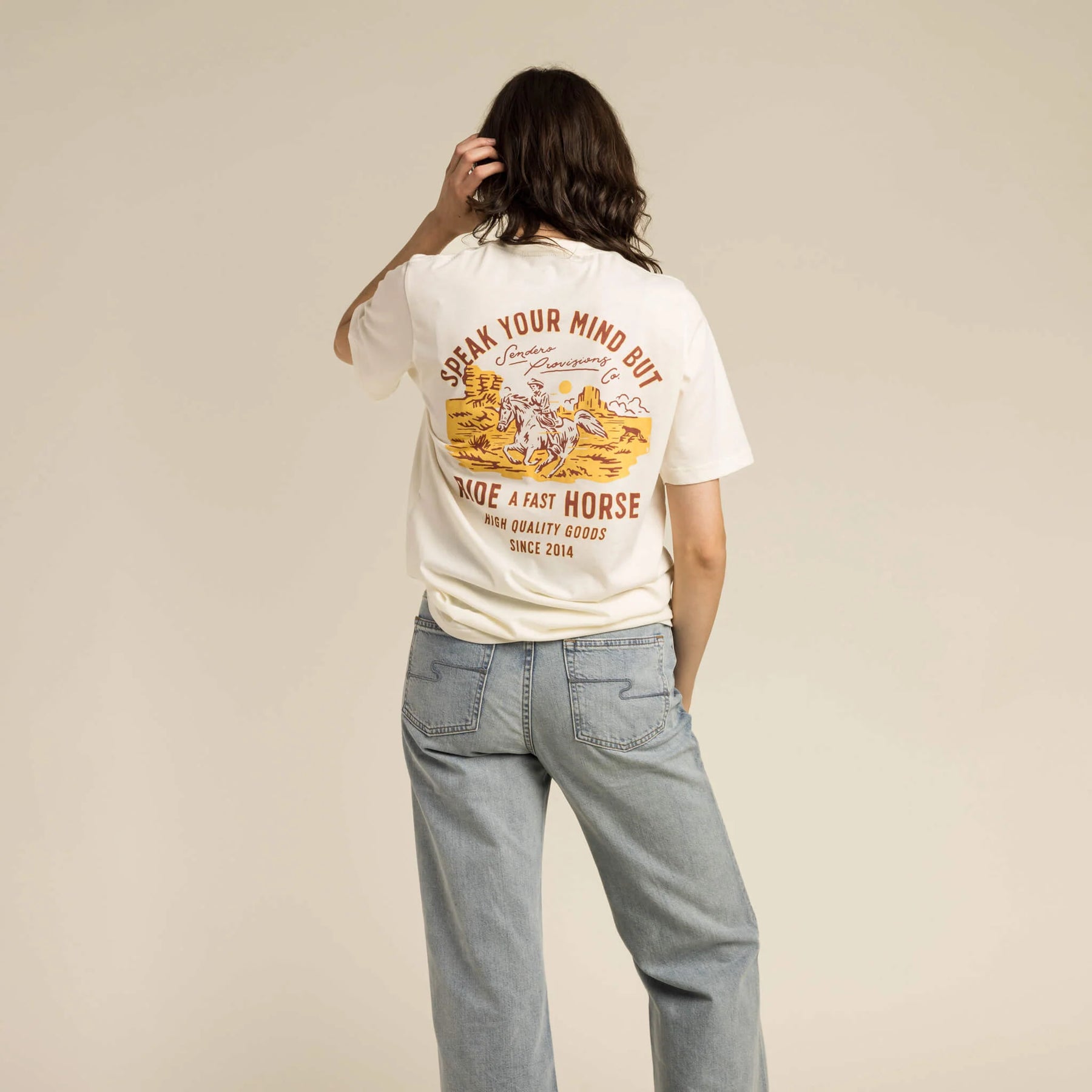 Person wearing a white t-shirt with a graphic and text, standing against a beige background